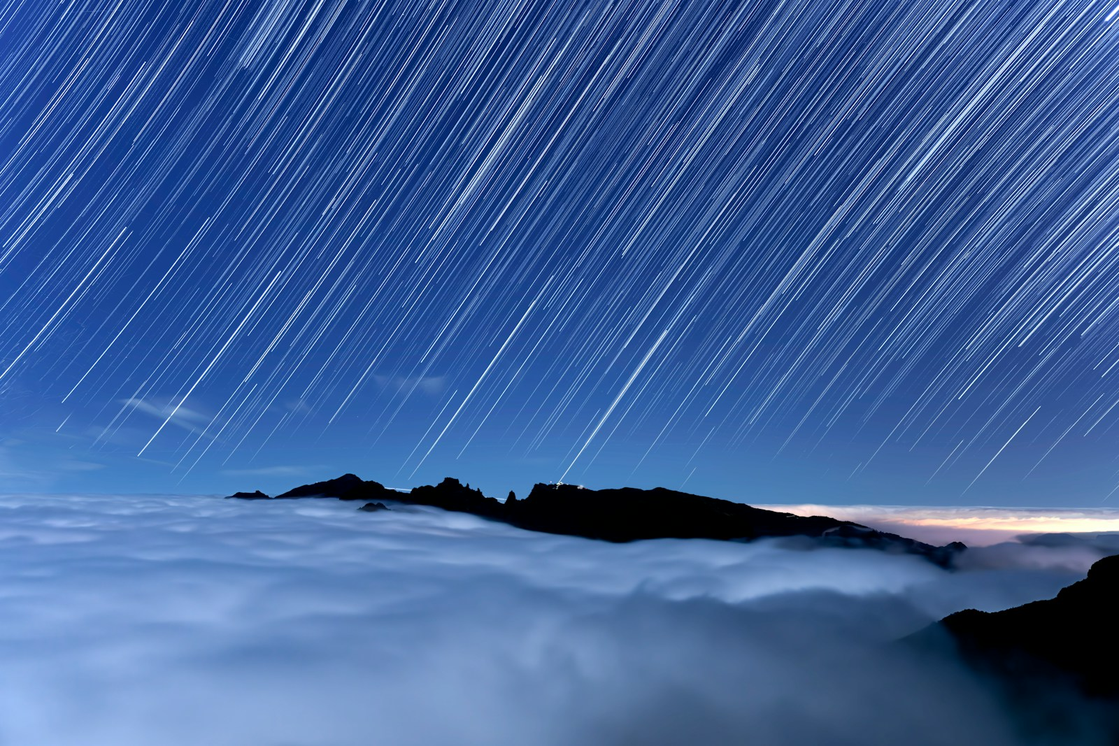 Star trails over clouds and mountain peaks at night
